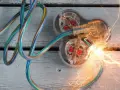 Des fils électriques colorés s'entremêlent, menant à une prise transparente où un court circuit provoque des étincelles vives.