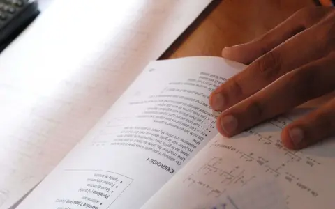 Main d'un étudiant sur un livre de maths, concentré sur le sujet maths jour 2. Formules et exercices à résoudre.