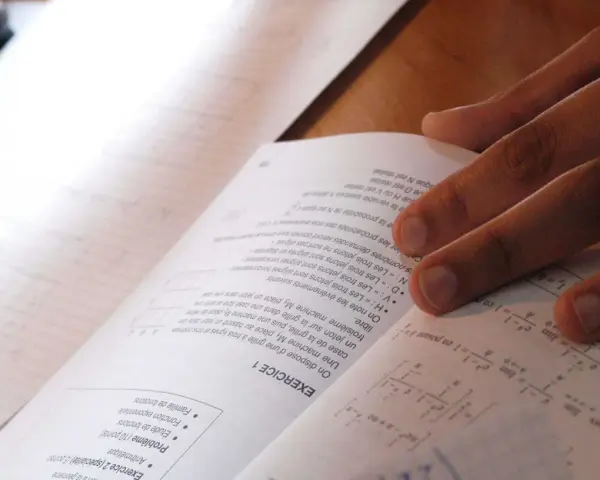 Main d'un étudiant sur un livre de maths, concentré sur le sujet maths jour 2. Formules et exercices à résoudre.