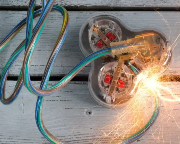 Des fils électriques colorés s'entremêlent, menant à une prise transparente où un court circuit provoque des étincelles vives.