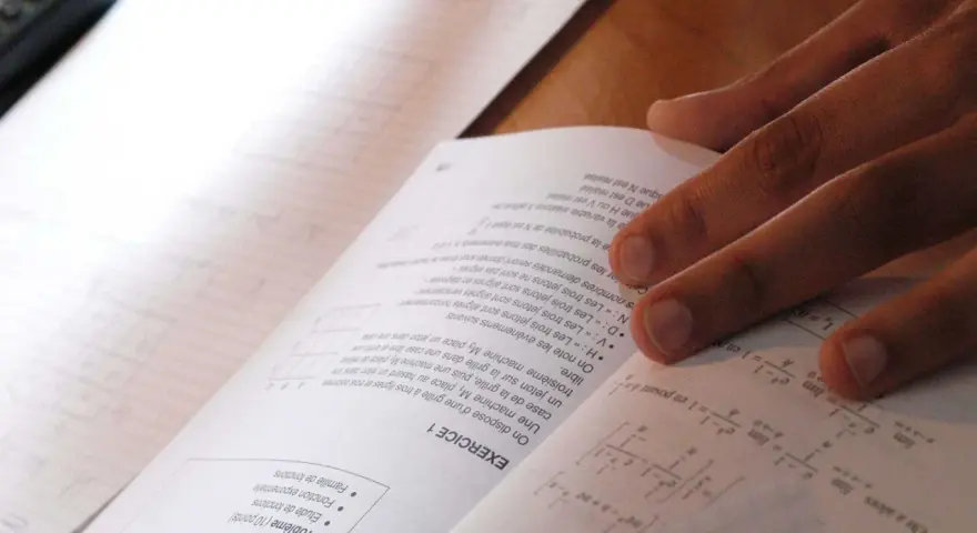 Main d'un étudiant sur un livre de maths, concentré sur le sujet maths jour 2. Formules et exercices à résoudre.