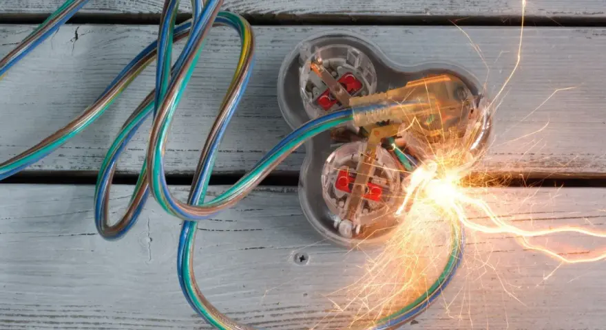 Des fils électriques colorés s'entremêlent, menant à une prise transparente où un court circuit provoque des étincelles vives.